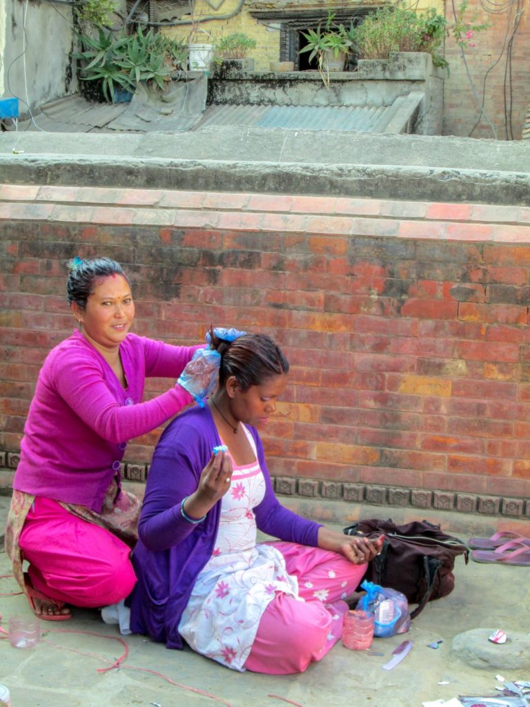 This is a photo of a women dyeing a customer’s hair in on the sidewalk.